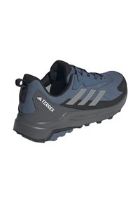 Zapatilla deportiva azul y gris con parte superior de textil, suela de goma y detalles de acento texturizados. Cuenta con tres rayas grises y una lengüeta.