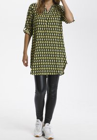 Camicia leggera a maniche lunghe con motivo a rombi verdi e neri, abbinata a leggings neri lucidi e sneakers bianche. Look casual e confortevole.