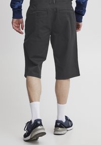 Șorturi gri cu un design plat în față, două buzunare dorsale și o lungime până la genunchi. Asortate cu șosete albe și pantofi sport închisi la culoare.