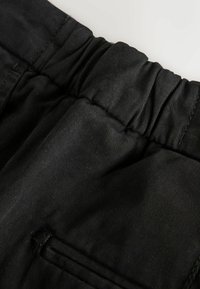 Black elastic waistband pants with a textured fabric, featuring a side pocket and soft finish. Subtle ribbing pattern throughout.