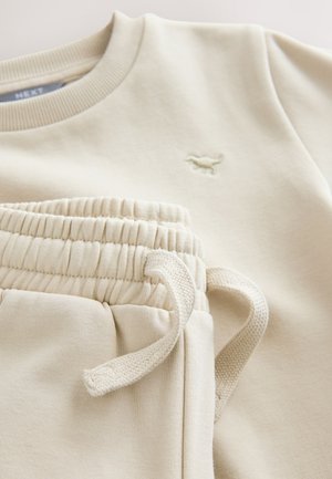 Beige bomuldssweatshirt med ribbet halsudskæring og broderet logo; matchende skræddersyede joggers med elastisk talje og snøre detalje.