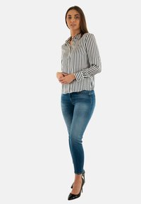 Camicia a righe con maniche lunghe, motivo in bianco e nero; abbinata a jeans skinny blu e tacchi alti neri.