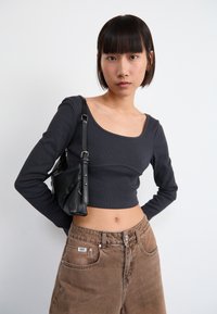 Black ribbed long-sleeve cropped top paired with brown high-waisted jeans. The model carries a small black bag with a shoulder strap.