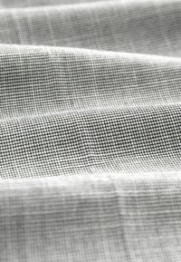 Grå och vit vävd tyg med ett litet rutmönster, som har en slät textur och en lätt lyster. Draperar mjukt.