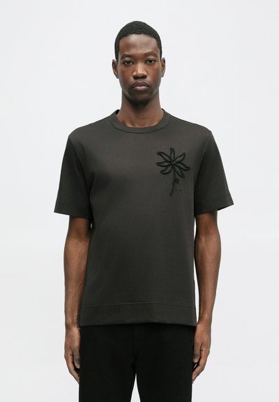 Tricou scurt cu mânecă, de culoare neagră, confecționat dintr-un material neted, având un design texturat cu flori pe partea stângă a pieptului. Guler rotund simplu și tiv drept.