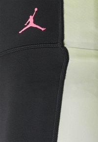 Czarne i jasnozielone legginsy sportowe z logo Jordana w kolorze różowym. Charakteryzują się gładką fakturą i widocznym szwem wzdłuż szwów.