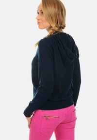 Sweat à capuche bleu marine avec une texture subtile, doté d'une poche kangourou et d'un ourlet côtelé, associé à un pantalon rose ajusté avec des poches zippées.