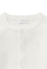 Vit stickad cardigan med rund halsringning, prydd med fyra krämfärgade knappar och ett litet broderat emblem på bröstet. Etiketten lyder "noppies."