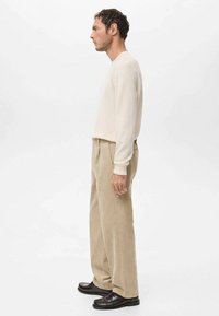 Suéter de punto beige claro con mangas largas combinado con pantalones de pana color crema. Destacan los zapatos de cuero marrón, diseño de corte recto y textura acanalada.