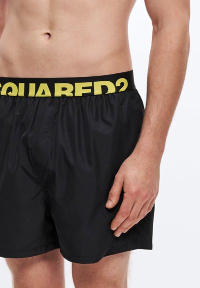 Fekete fürdőnadrág sárga rugalmas derékpánttal, amelyen "SQUARED2" felirat található. Az anyag sima és könnyű, elasztikus szabással.