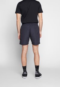 T-shirt noir pour homme, shorts bleu marine et chaussures noires avec des chaussettes. Les shorts ont une taille élastique et un tissu lisse. Design simple, sans motifs.