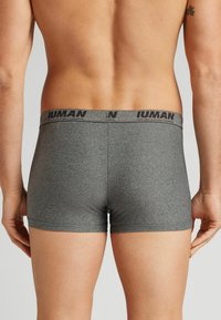 Boxer shorts de tela elástica gris con una cinturilla de logotipo negro. Diseño ajustado con textura suave y costuras mínimas.