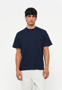 Marineblauwe t-shirt met korte mouwen van katoen, met een ronde hals en geborduurd logo op de linker borst. Glad textuur, recht gesneden.