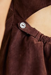 Bruine leren kledingdetail met een gestructureerd oppervlak, knoopsluiting en geraffineerde stof voor extra diepte.