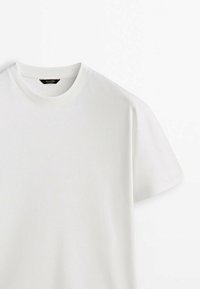 T-shirt blanc uni en coton à manches courtes, col rond côtelé et étiquette de marque noire à l'intérieur du col.
