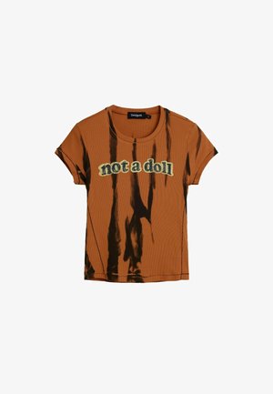 Pruun soonikuga t-särk musta lipsuvärvilaigulise mustriga, ümar kaelus, üleskeeratud varrukad ja kollase ning musta värviga „not a doll“ tekst esiküljel.