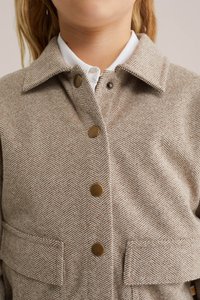 Brūns herringbone raksta žakets ar apkakli, pogu aizdari un diviem priekšējiem kabatām. Satur misiņa pogas un teksturētu audumu.