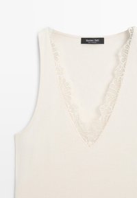 Crèmekleurige geribde mouwloze top met V-hals afgewerkt met fijne kant, met een Massimo Dutti-label aan de achterkant van de halslijn.