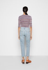 Mångfärgad ribbad stickad topp med trekvartslånga ärmar, som matchas med ljusblå slitna jeans och bruna klacksandaler.