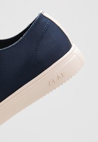 Chaussure en toile bleu marine à enfiler avec une tige texturée, une semelle en caoutchouc blanche et un logo discret sur le côté. Design minimaliste avec des accents contrastants.