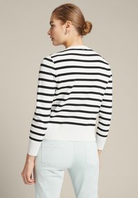 Schwarz-weiß gestreifter Pullover mit geripptem Saum und Bündchen, mit Rundhalsausschnitt und figurbetontem Design. Getragen mit hellblauen Jeans.
