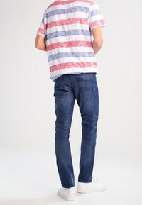 Randig t-shirt med röda och blå vågor, blå jeans och vita sneakers. Tröjan har rundad nederkant och korta ärmar; jeansen är slim-fit.