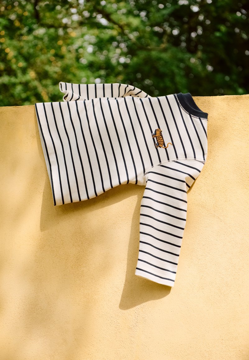 Kreemikas ja mereväes triibuline pikkade varrukatega särk, millel on väike tiigri tikand, valmistatud pehmest kangast, lõdva istuvuse ja ümmarguse kaelusega.