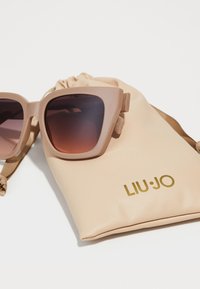 Beige oversized sunglasses with gradient brown lenses, resting on a matching beige drawstring pouch featuring gold lettering "LIU•JO."