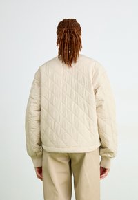Giacca bomber beige imbottita con polsini e colletto a costine, caratterizzata da una vestibilità rilassata e un motivo testurizzato, abbinata a pantaloni beige coordinati.