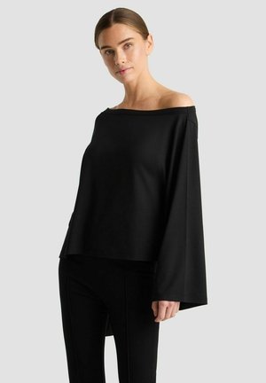 Zwarte off-shoulder top gemaakt van zachte stof, met een losse fit en brede mouwen. Gecombineerd met zwarte fitted pants.