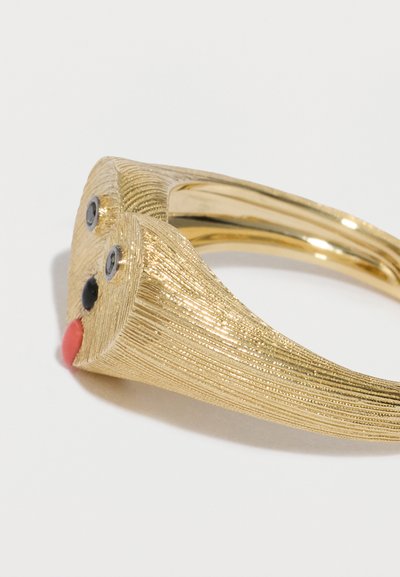 Náramok v zlatej farbe s textúrovaným povrchom, tvarovaný do podoby tváre s dvoma čiernymi očami, červeným jazykom a zakrivenou štruktúrou.