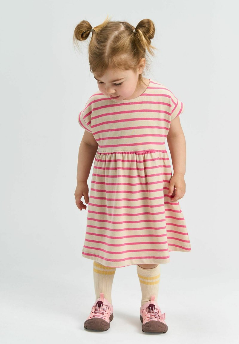 Robe rayée beige et rose, à manches courtes, taille froncée. Accompagnée de chaussettes rayées jaunes et crème et de baskets roses.