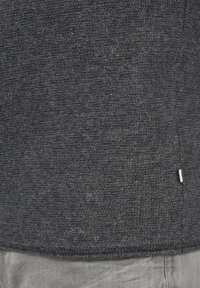 Suéter de punto gris oscuro con una tela texturada, que presenta un detalle de costura y una pequeña etiqueta blanca en el dobladillo.