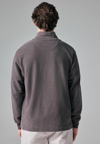 Pull-over à manches longues en gris foncé, avec un col polo, un tissu texturé et un design à épaules tombantes. Coutures visibles à l'ourlet et aux coutures.