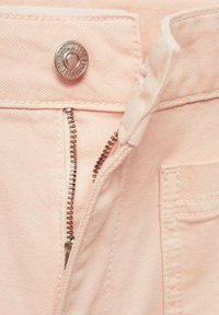Jean en denim rose clair avec un bouton en métal et une braguette partiellement ouverte, montrant le coin supérieur de la poche avant.