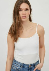 Top blanco sin mangas con un diseño ajustado y textura suave, combinado con unos pantalones cortos de mezclilla azul de cintura alta. Estilo claro y sencillo.
