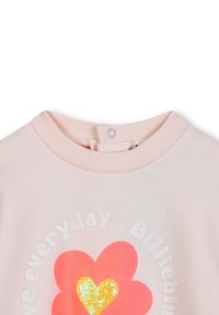 Sweatshirt rose clair avec un col rond. Présente un texte blanc et un grand cœur rouge avec des accents jaunes et des paillettes. Texture de tissu douce.