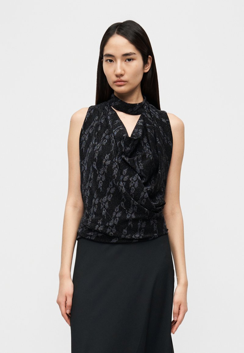 Μαύρο αμάνικο τοπ με εμπρός μέρος που πέφτει σε π τυχές, με λαιμόκοψη τύπου κλειδαρότρυπα. Το ύφασμα έχει διακριτική λαμπερή υφή και σχέδιο με αχνές αφηρημένες απεικονίσεις.