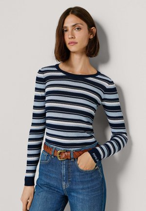 Ribidega pikkade varrukatega pluus mereväe, helesiniste ja valgete horisontaaltriipudega. Sobitatud kõrge vöökohaga siniste teksapükstega ja pruuni palmikutriibulise vööga.