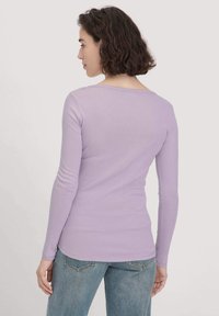 Lila langomshirt met een zachte textuur en een ronde halslijn, gecombineerd met lichte denim jeans. Het ontwerp is strak en soepel.