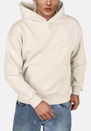 Sudadera color crema hecha de tela suave, con un bolsillo tipo canguro y puños de canalé. Detalle sutil del logo en el pecho.