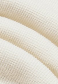 Tela de crema texturizada que muestra un patrón acanalado, exhibiendo una apariencia suave y tejida con un estiramiento elástico.