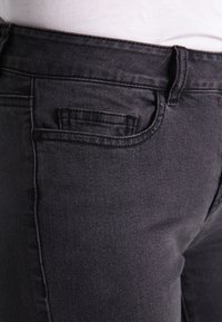 Tmavě šedé džíny z denimu, s přiléhavým střihem, obsahující malou přední kapsu a jemné švy podél švů. Texturovaná látka.