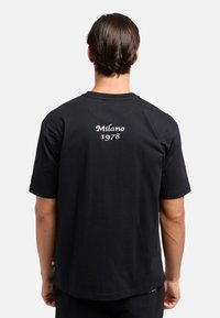 Zwarte katoenen T-shirt met een ronde hals en korte mouwen. De achterkant toont "Milano 1978" in witte borduursel. Eenvoudig ontwerp zonder patronen.