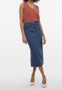 Haut rouge rustique sans manches associé à une jupe en denim taille haute, longueur au genou. La jupe comporte une fente à l'avant et un design classique en jean bleu.