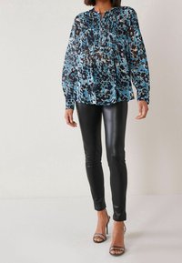 Sinistä ja mustaa leopardi-kuosisia blouseja, joissa on poimutettuja yksityiskohtia, pitkät hihat ja pyöreä kaula-aukko, yhdistettyinä mustiin synteettiseen nahkaan tehtyihin leggingsseihin ja nyörillisiin korkokenkiin.