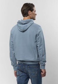 Svetlo modra bombažna jopa s kapuco zadaj, rebrastimi manšetami in spodnjim robom, združena z modrimi kavbojkami z zadnjimi žepi in bledenim vzorcem.