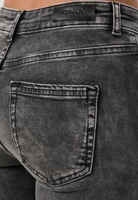 Grå denim jeans med en falmet tekstur, der har en baglomme og et sort læderlogo på bagkanten.