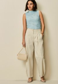 Ljusblå stickad ärmlös topp i kombination med högmidjade beige byxor, strappy nude klackar och en lätt vadderad väska.