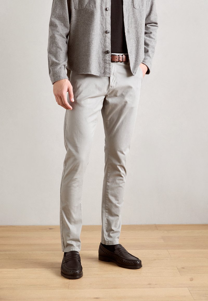 Gray button-up shirt over a black top, paired with light gray trousers and dark brown loafers. Smooth fabric with subtle texture.
